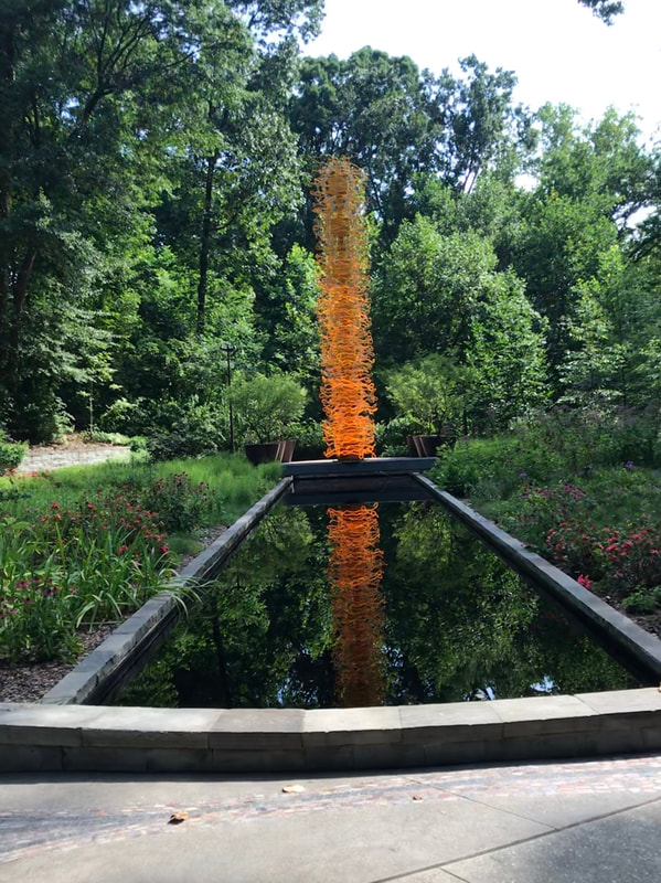 A tall orange sculpture with lights stands at the end of a dark reflecting pool.
